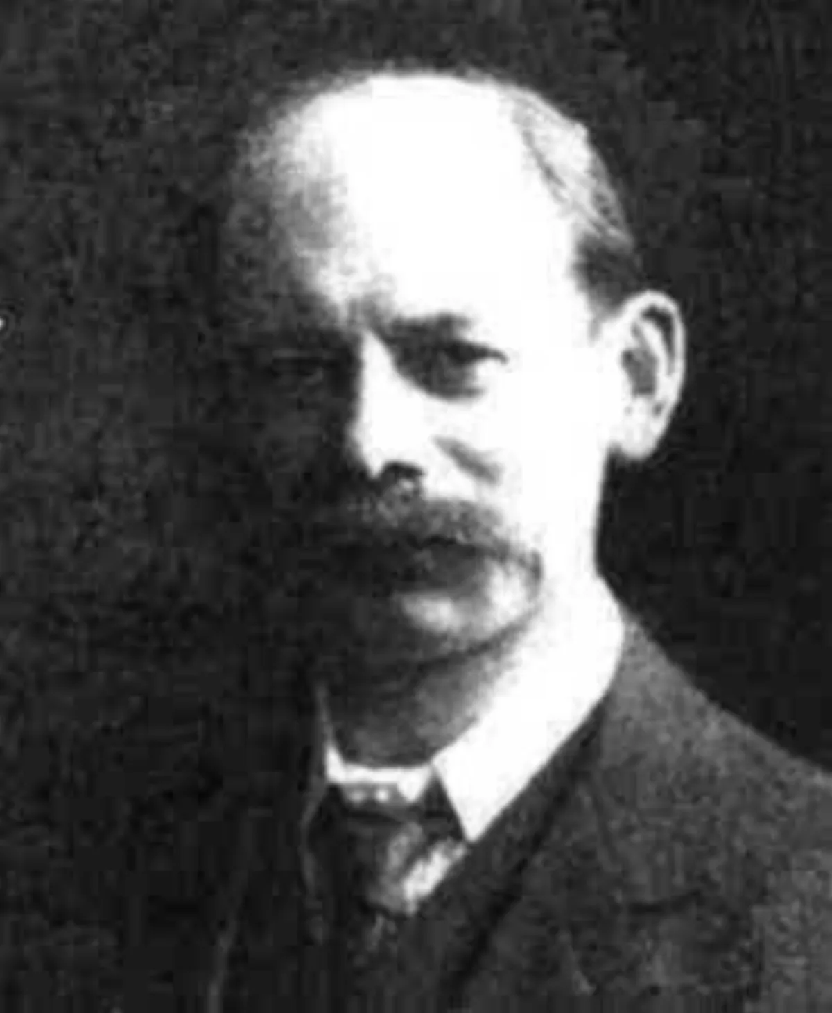 A black and white portrait of an elderly man with a large walrus moustache, shown from the shoulders up.