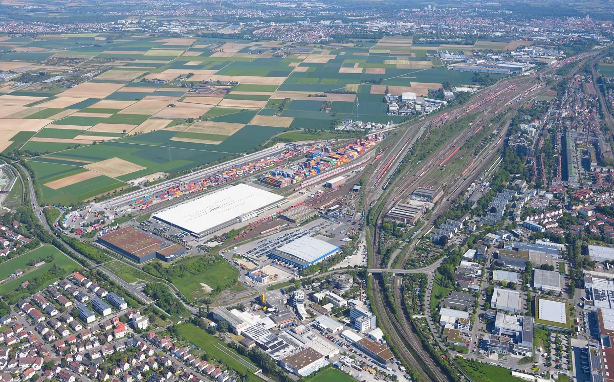Oblique aerial photograph of a rail yard: a broad bundle of parallel tracks running down the right-hand side, with fields, houses and stacked shipping containers around it.