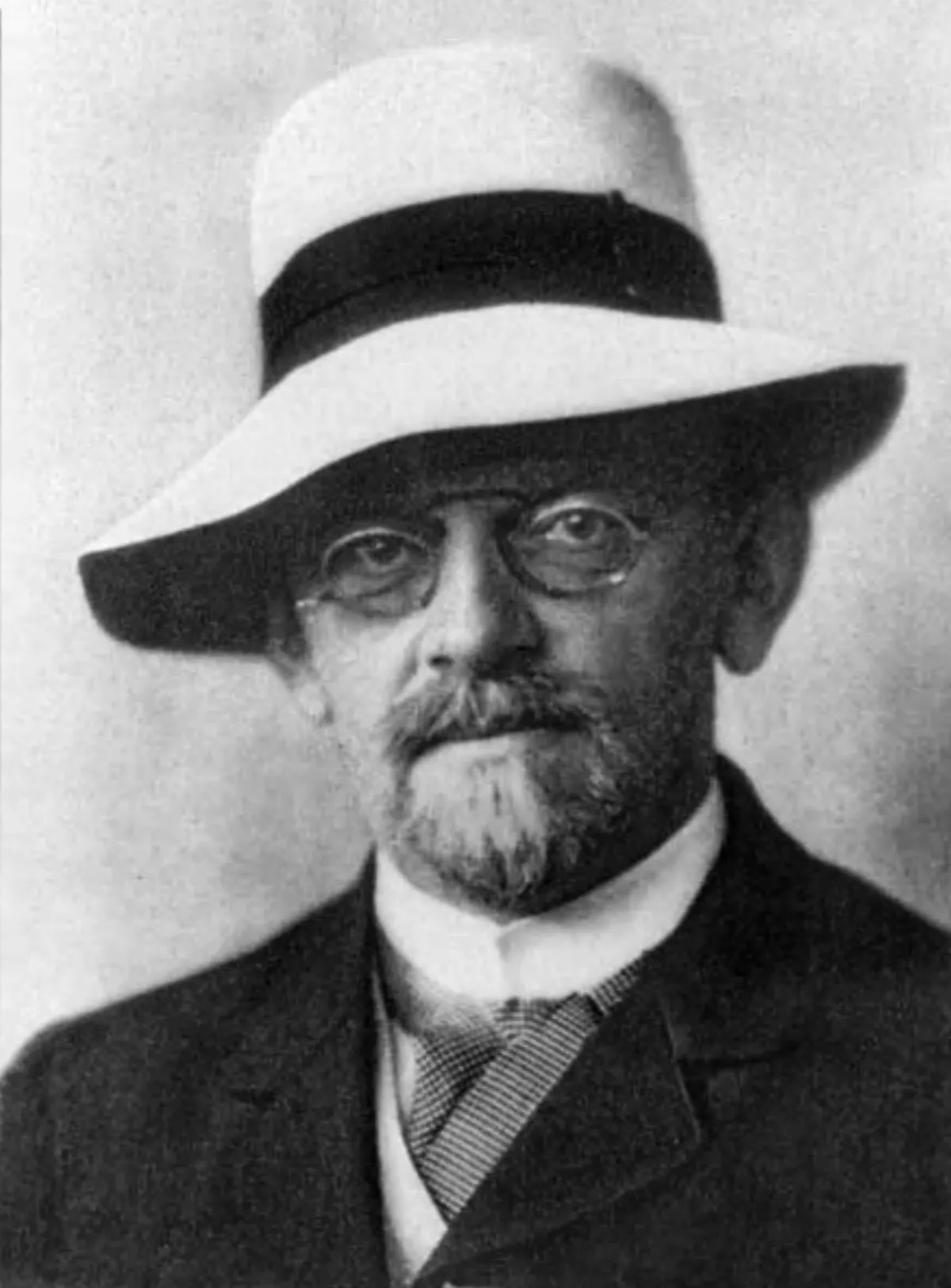 Black-and-white portrait photograph of a bearded man in a hat and spectacles, facing the camera.