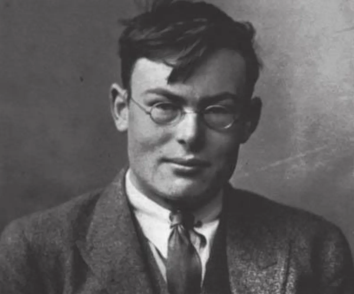 A black-and-white photograph of a young man in round wire-rimmed spectacles and a tweed jacket.