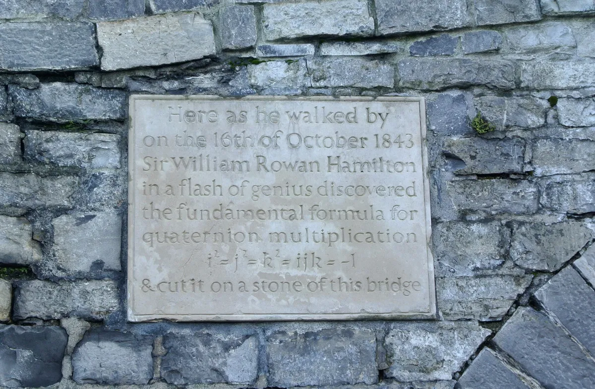 A stone plaque with an engraved inscription set into the rubble stonework of a bridge parapet.