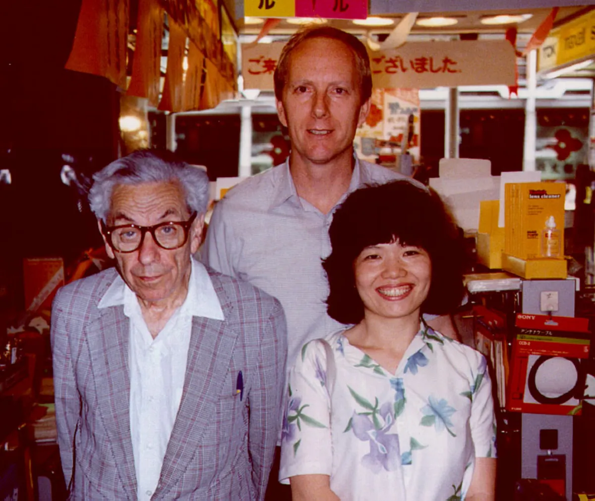 Colour photograph of three people standing side by side in a shop, with shelves of boxed electronics behind them.