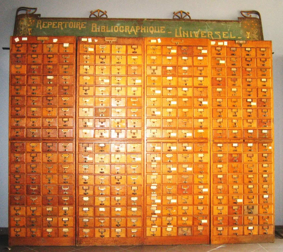 Four tall banks of small labelled wooden drawers beneath a painted sign reading Repertoire Bibliographique Universel.